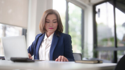 Obraz premium Asian businesswomen reading marketing business report to checking financial chart data and typing data on keyboard laptop while analyze investment and market stock of new startup in outside office