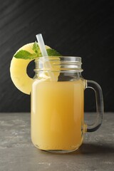 Tasty pineapple juice in mason jar, mint and slice of fruit on grey textured table, closeup