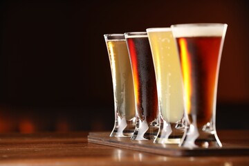Glasses with different types of beer on wooden table against color background, closeup. Space for...