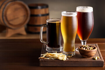Glasses with different types of beer and snacks on wooden table in bar. Space for text
