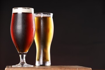 Glasses with different types of beer on board against black background, closeup. Space for text