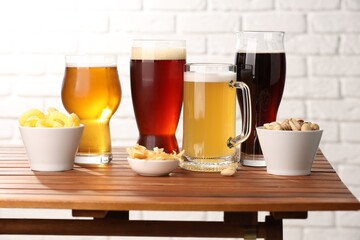 Glasses with different types of beer and snacks on wooden table against white brick wall
