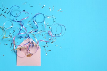 Shiny confetti and party streamers flying out of envelope on light blue background, flat lay. Space for text