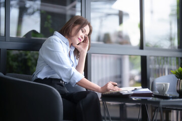 Asian businesswomen reading marketing document to thinking about planning of new business and taking notes in notebook while analyzing investment and market stock of new startup in outside office