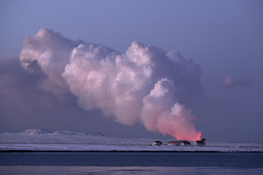Snowy mountains and cloudy smoke erupting from burning volcano