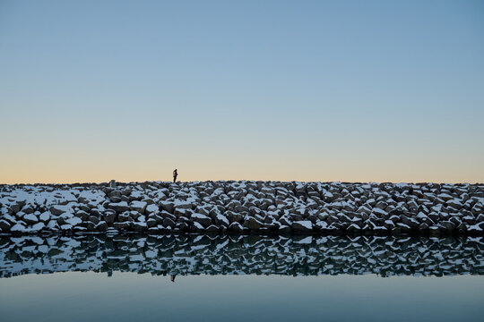 Silhouette of unrecognizable person standing on lake shore with rocks