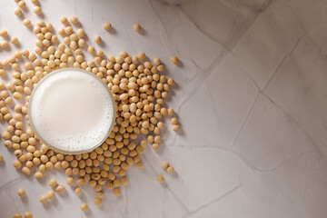 Top shot of fresh soy milk in a glass surrounded by scattered soybeans on marble background. 