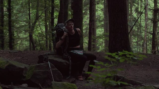 girl putting on heavy backpack in forest