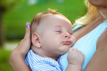 A peaceful baby nestles in a mother’s embrace, enjoying a tranquil nap beneath a clear blue sky,...
