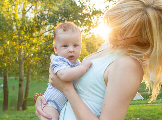 A mother tenderly cradles her baby on a sunny afternoon in a lush park, surrounded by vibrant...