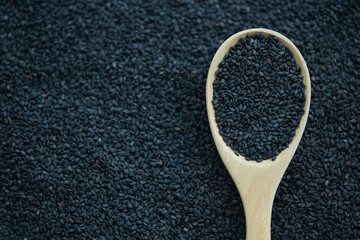 Black sesame seeds in wooden spoon on black background