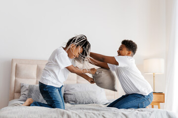 Happy two kids playing on the bed in the bedroom, using pillows