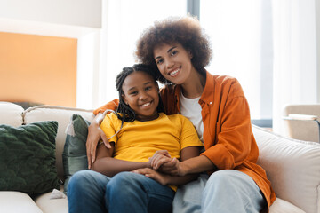 Happy young African American woman embracing with her daughter, looking at camera