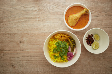 Top view of Rice noodle with chicken and curry in white bowl on wooden background, Khao soi a famous northern Thai food