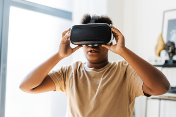 Amazed African American boy using VR headset while playing at futuristic game at home