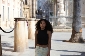 beautiful young latin woman with dark eyes and long curly hair walks through the centre of Seville, in the background you can see the cathedral of catholic worship and gothic style of Seville, Spain.