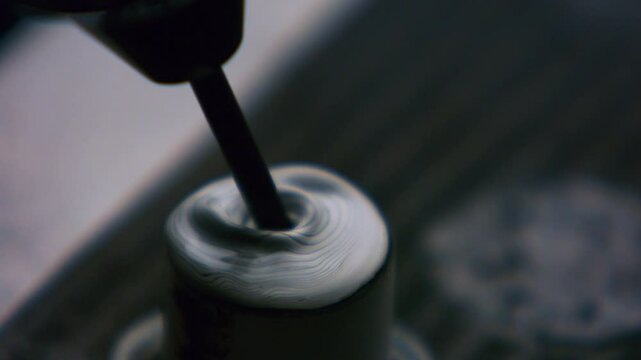 Clouseup of tattoo artist mixing ink in caps fixed with vaseline on table. Tattooist preparation, flow of dark fluid dye in container. Master tattooer loads flask with ebony paint liquid.
