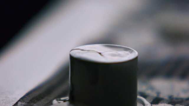 Clouseup of tattoo artist mixing ink in caps fixed with vaseline on table. Tattooist preparation, flow of dark fluid dye in container. Master tattooer loads flask with ebony paint liquid.