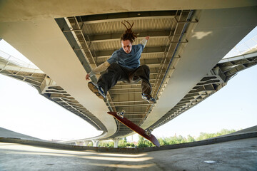 Skateboarder performing trick under large overhead bridge showing skill and agility mid-air with...