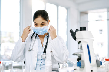 Woman, doctor and mask with microscope for forensic, science or medical discovery at laboratory. Female person, biologist or scientist with protection for chemical, virus or health and safety at lab