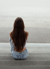 Back view of a young woman sitting on the stairs in urban environment