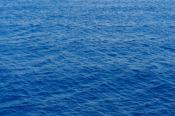 Serene view of the calm ocean water, natural texture and color of the sea under clear skies. Small ripples on still water surface. Summer daylight
