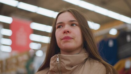 Close-up of a young girl in a brown jacket, looking around in a mall. The background is blurred, emphasizing her curious and observant expression