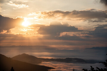 Majestic Mountain Landscape Covered in Mist with Sun Rays Breaking Through Clouds