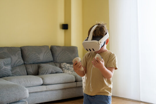 Excited child with virtual reality glasses in the living room at home. School education program for children. Surprised little boy looking with VR glasses