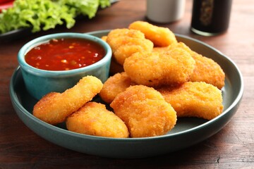 Plate with hot chili sauce and nuggets on wooden table, closeup