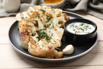 Delicious grilled cauliflower steaks with sauce, garlic and dill on wooden table