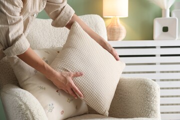 Woman putting soft pillow onto light armchair in living room, closeup