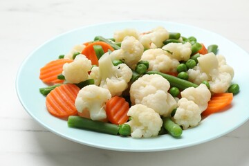 Tasty cooked cauliflower with green peas, string beans and carrot slices on white marble table, closeup