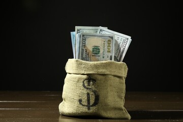Dollar banknotes in sack on wooden table against dark background