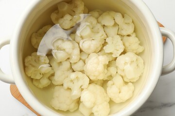 Cauliflower in pot with water on white marble table, top view