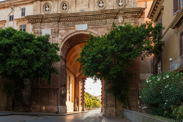 Obraz premium Close-up view of the archway of Porta Nuova in Palermo, Sicily, highlighting detailed stonework and decorative elements, framed by trees and illuminated by sunlight