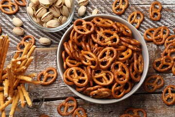 Delicious pretzel crackers, salty sticks and pistachios on wooden table, flat lay