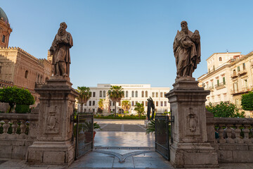 View through gate flanked by statues near Palermo Cathedral in Sicily, historical architecture and the Liceo classico Vittorio Emanuele II building in background