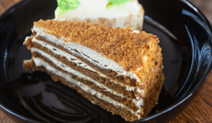 A honey cake on a black plate next to a piece of another cake close-up