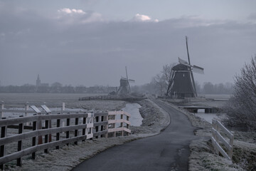 The dramatic scene with a Dutch windmill in a foggy and cold winter weather