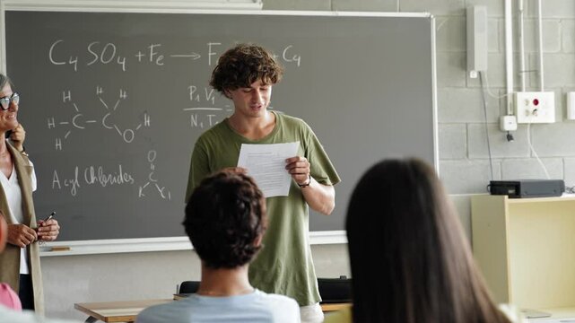College student presenting a project reading a presentation to classmates and teacher at High School classroom