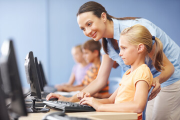 Woman, teacher and smile with girl on computer in classroom for helping, teaching and learning. People, educator and happy online with student at elementary school for education and brain development