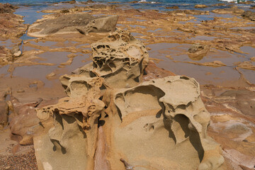 Natural sandstone rock formations with intricate erosion patterns on a coastal shoreline, creating a unique and rugged landscape near the water
