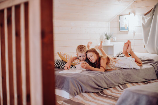Children, brother and sister play on smartphone in children's room. Happy children lie on bed and hang out in gadgets. Parental control, online education of children, communication in social networks