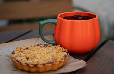 Rosehip warm tea in an orange pumpkin mug with a delicious apple tart on a wooden table. Close view.