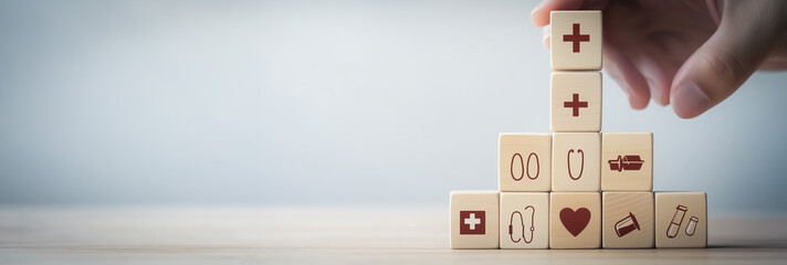 Hand placing healthcare-related icons on wooden blocks, building a structure that represents the importance of health, care, and wellness.