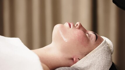 Close-up of a cosmetologist applying a cosmetic peeling mask to a client's face. The scene emphasizes the professional approach to skin care and the relaxing spa experience.