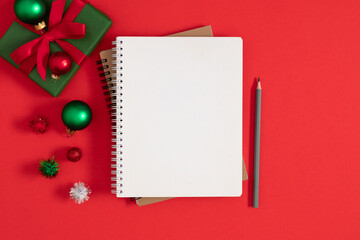 Christmas concept. Xmas checklist or invitation on red table. Blank notebook with pencil and christmas decorations on red background. Top view and space for your text. Flat lay.
