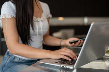 A close-up of an Asian woman working on her laptop, typing on the laptop keyboard.