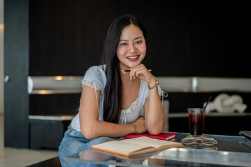 An attractive Asian woman sitting in a coffee shop, smiling at the camera.